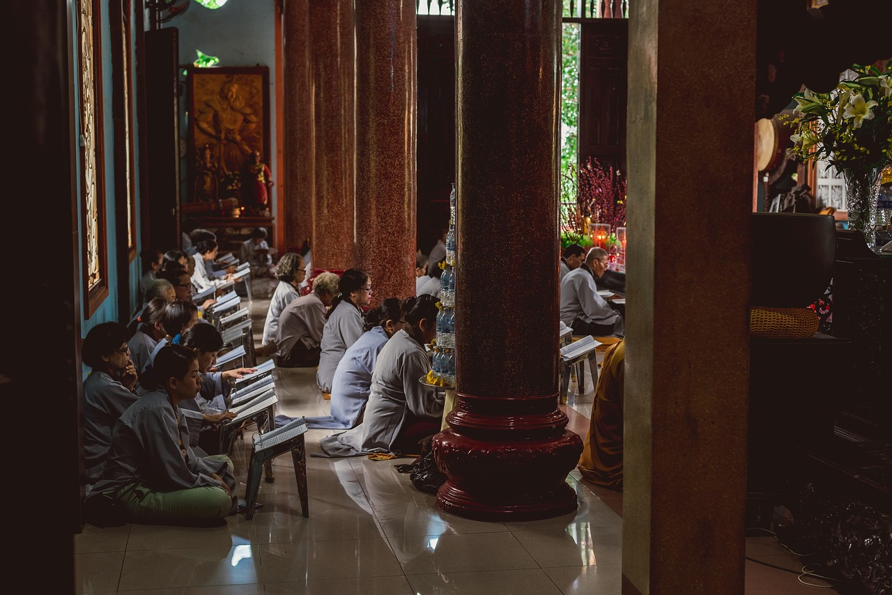 Vietnamese devotees in gray robes sitting cross-legged, reciting prayers in a pagoda in Hanoi