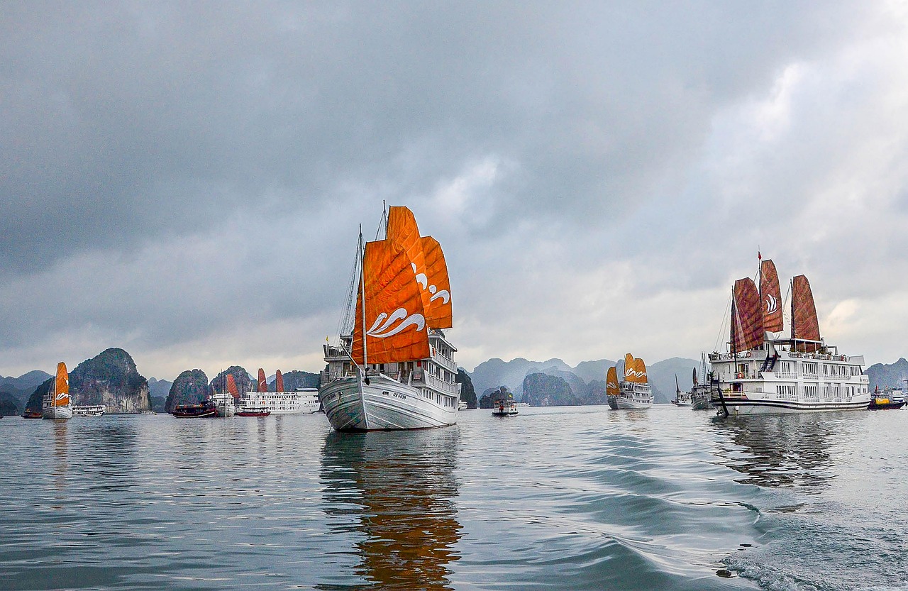 Orange-sailed junk boats sailing through Ha Long Bay under a heavy grey overcast sky