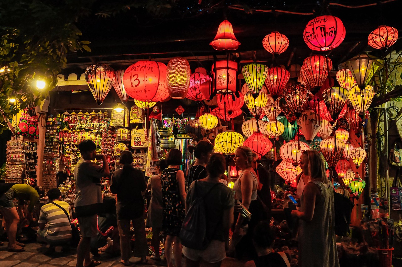Tourists browsing a Hoi An old town stall entirely covered in lit red and yellow silk lanterns at night