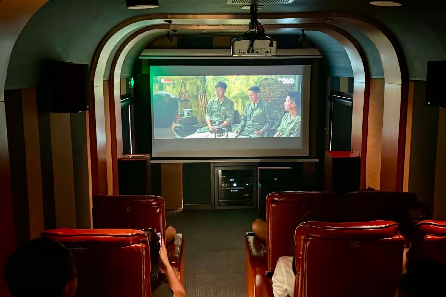 Salle de projection du train Huế – Phong Nha : fauteuils en cuir rouge face à un grand écran qui diffuse un film
